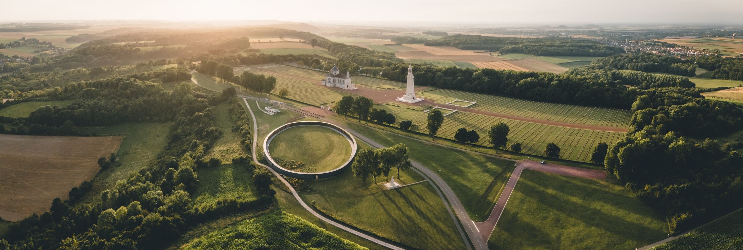 Aerial panoramic view of a circular monument surrounded by lush green countryside landscape.