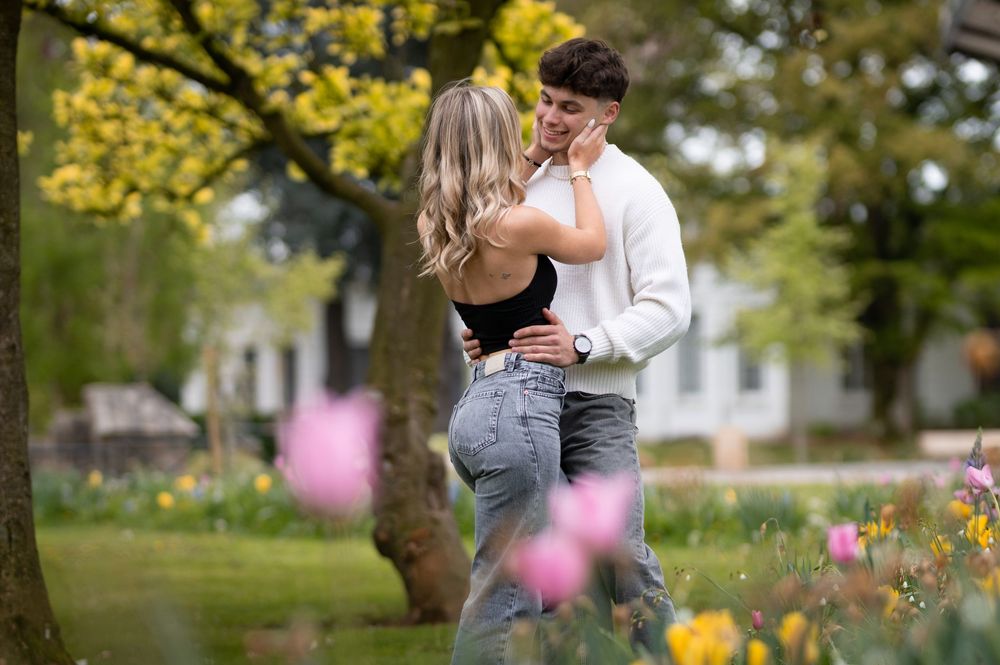 Young couple share a romantic moment in a blooming spring garden surrounded by colorful tulips and yellow trees.