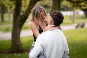 Couple sharing a romantic moment in a green park, woman smiling as man holds her close.