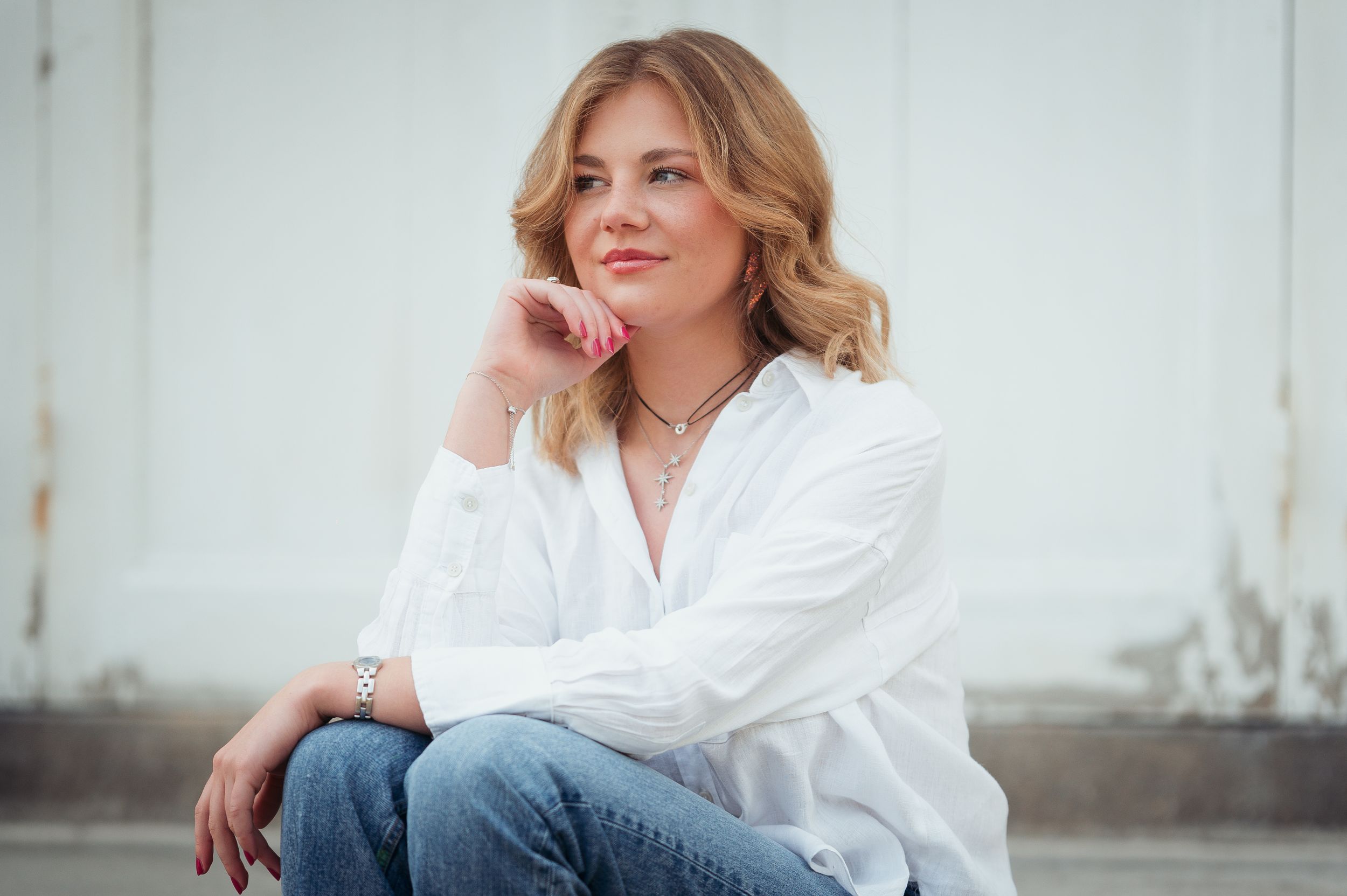 Un portrait décontracté en extérieur, avec une chemise blanche à boutons et un jean, sur un fond clair.