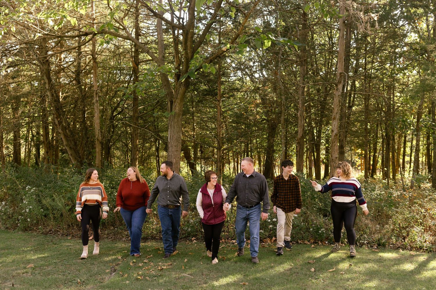Group of people walking in a line through a lush green forest setting.