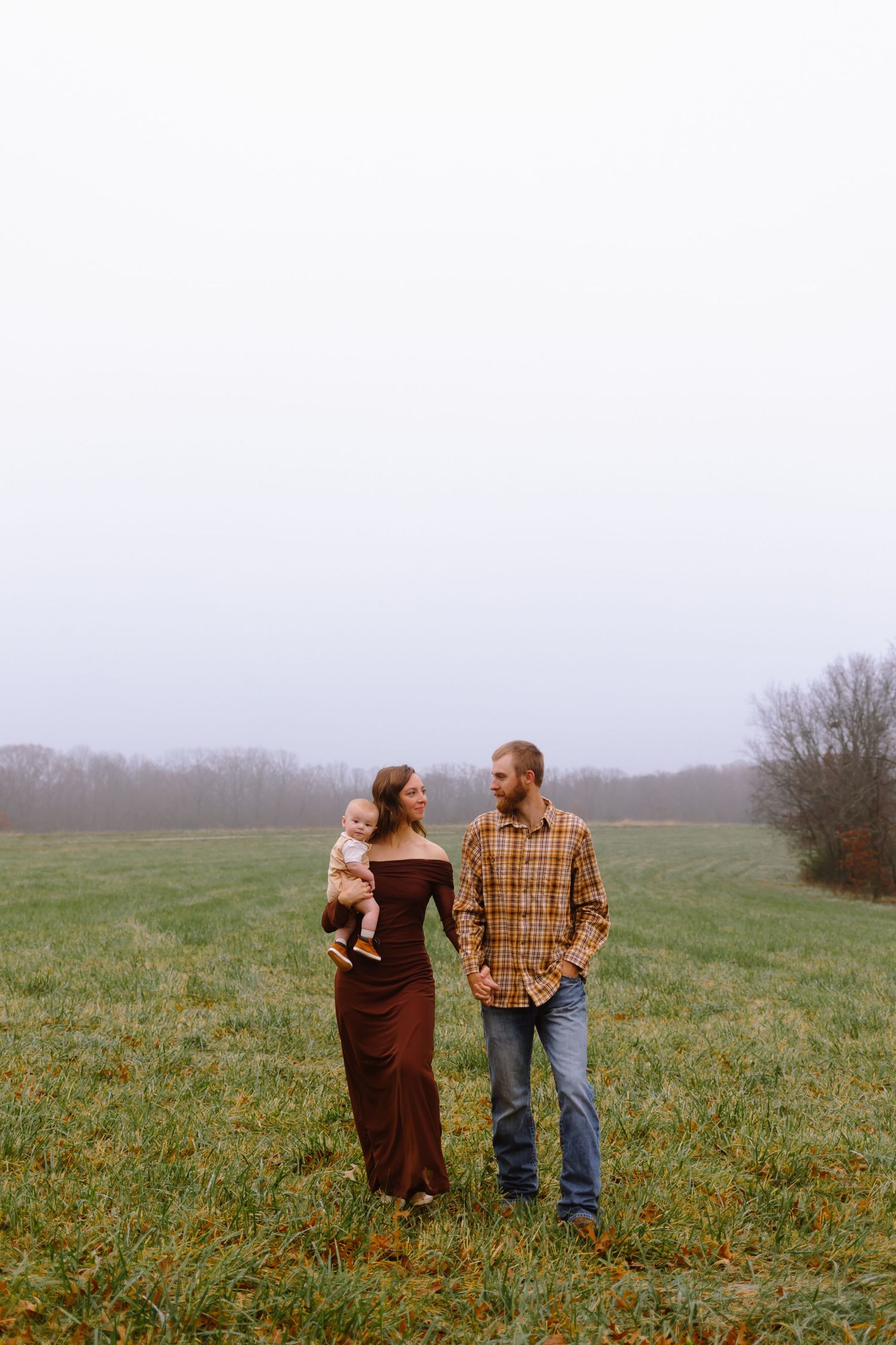 A couple stands together in a misty green field on an overcast day.
