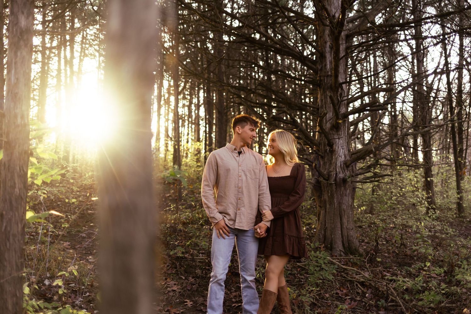 A couple shares an intimate moment in a sunlit forest during a romantic photoshoot at golden hour.