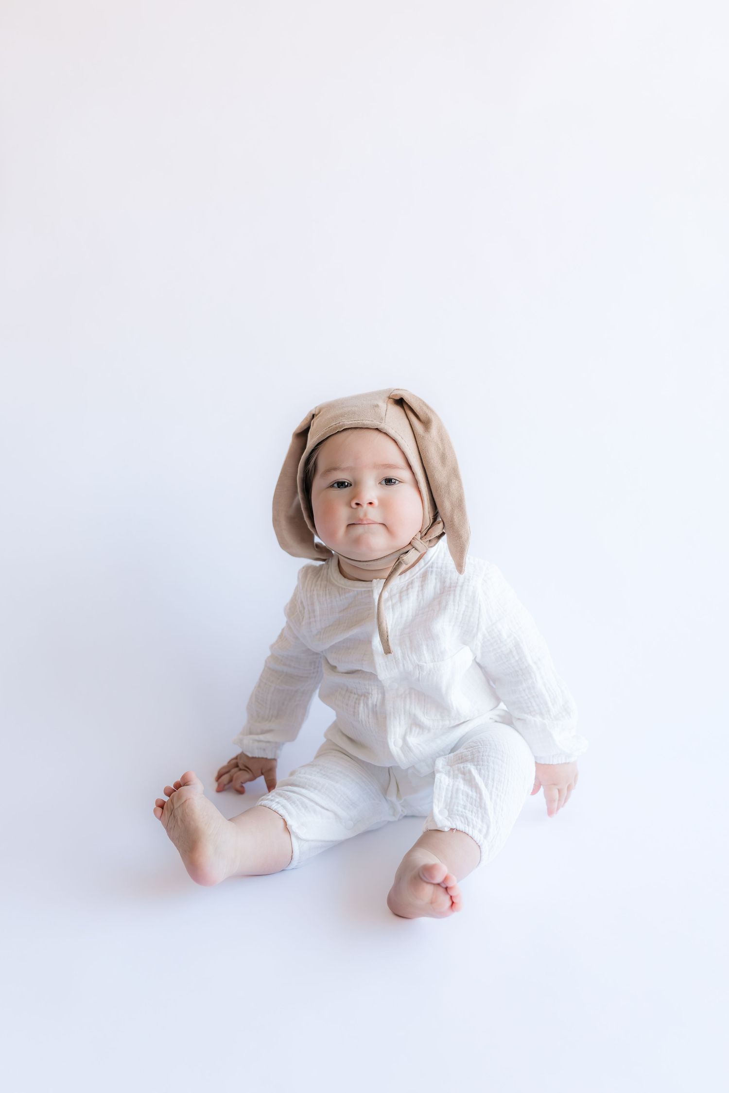 Baby in white outfit wearing bunny ears crawls on white background in three progressive movement shots.