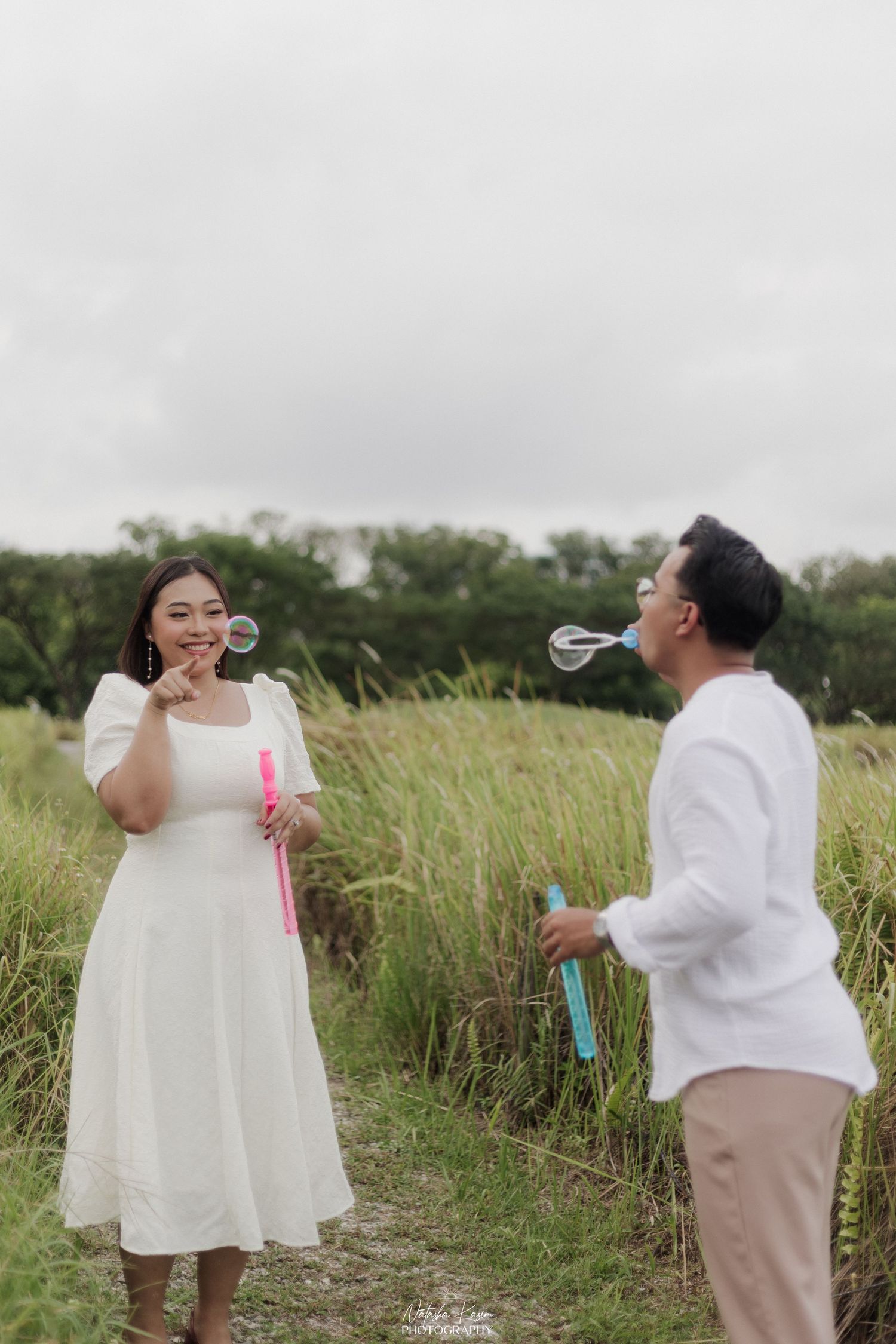 Two people in coordinated white outfits walk and interact playfully on a garden path.