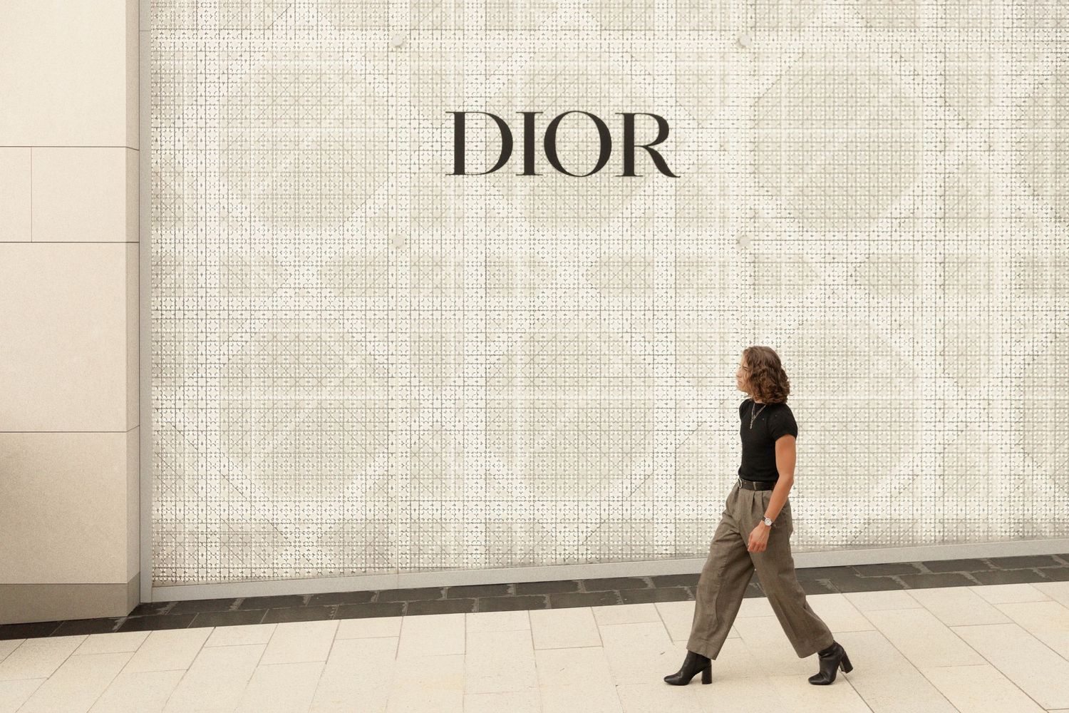 A minimalist scene of someone walking past a white wall with DIOR signage.