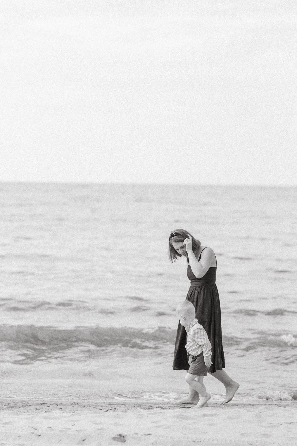 Black and white photograph of someone walking along the beach and dipping their feet in the ocean water.