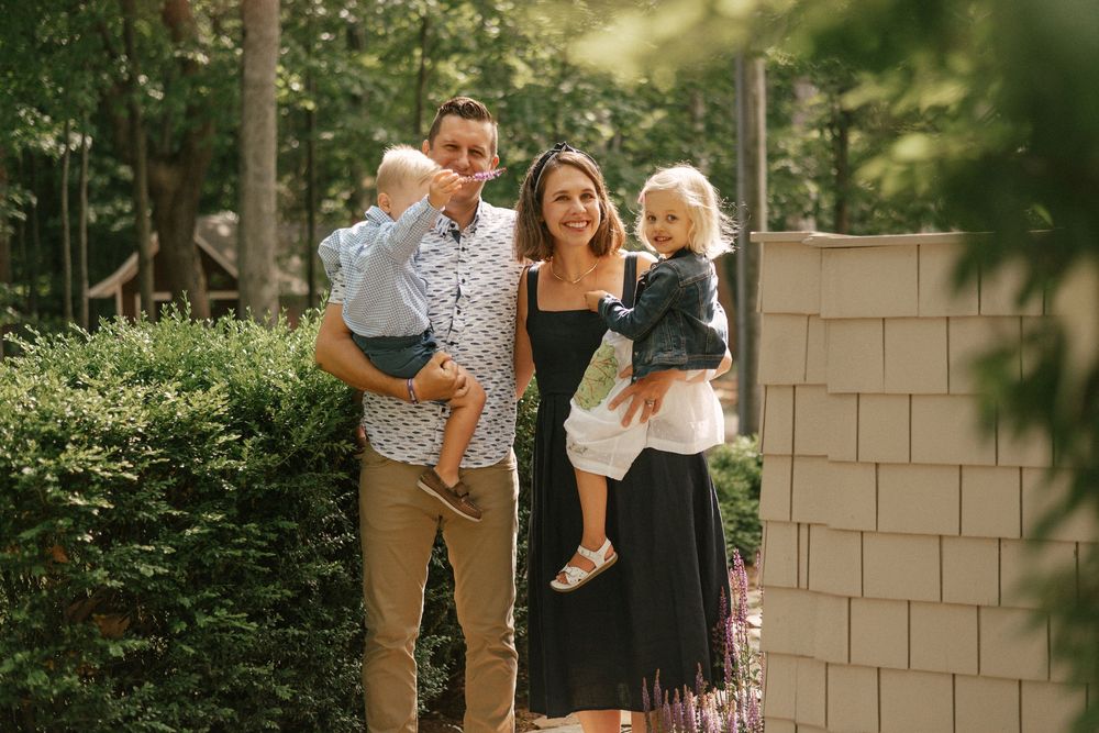 A happy family poses together outside their home on a sunny afternoon, framed by greenery and natural light.
