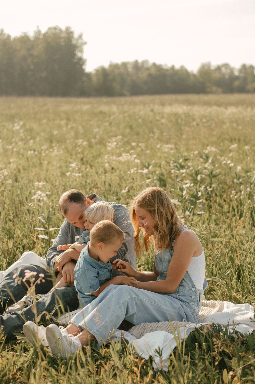 Family enjoying a summer picnic together in a golden meadow at sunset with white wildflowers all around.
