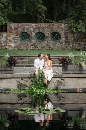 Couple sits together by a reflective lily pond in front of a stone garden wall.