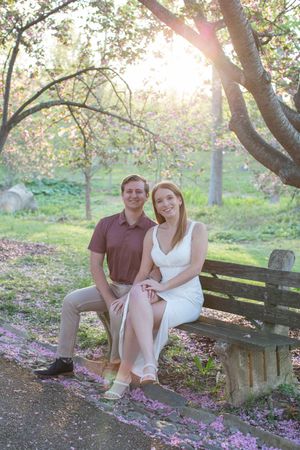 Couple sitting on a wooden bench under blooming cherry blossom trees in a sunlit park during spring.