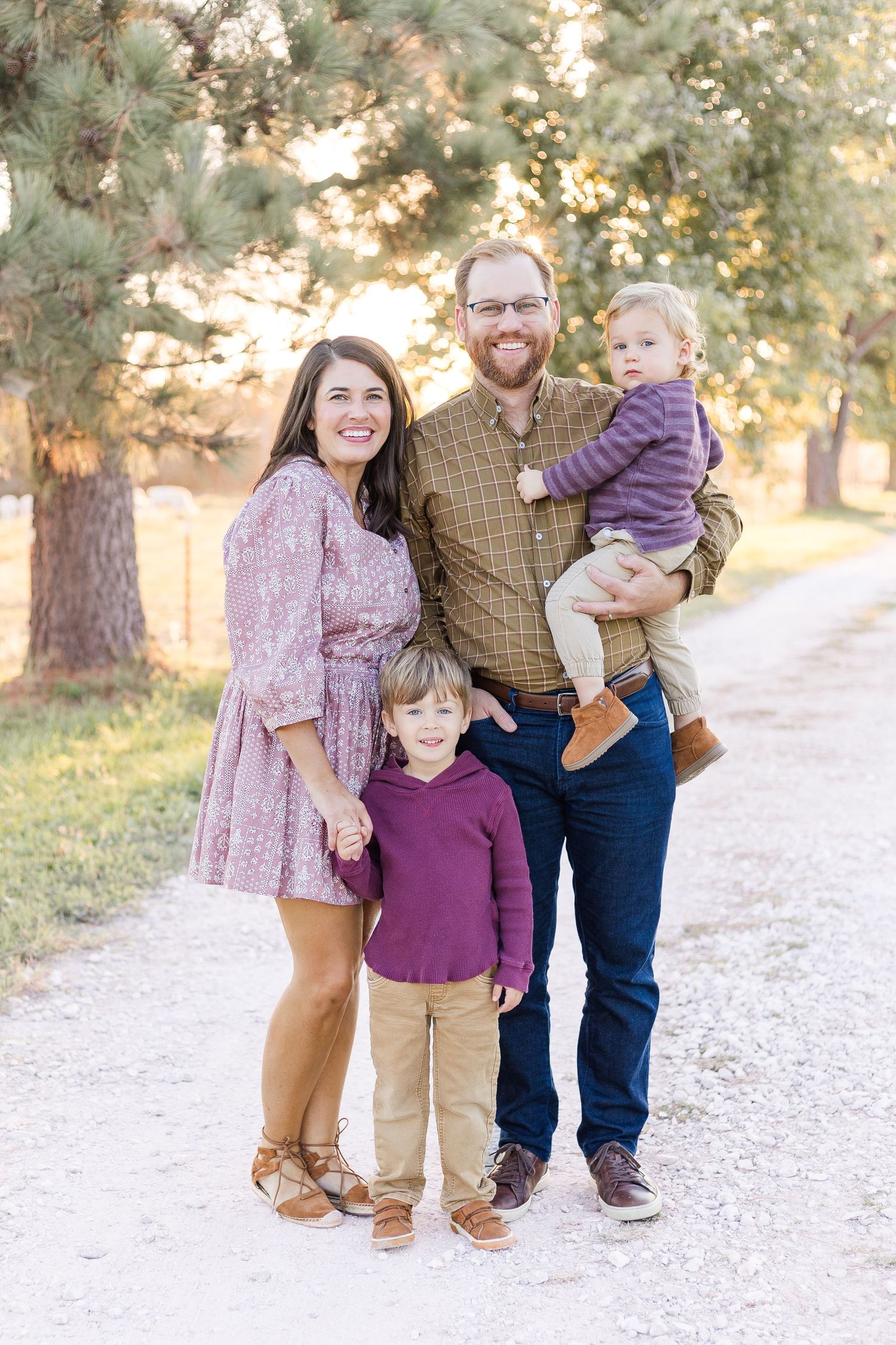 Family of four posing together on a tree-lined pathway during an outdoor family portrait session in autumn.