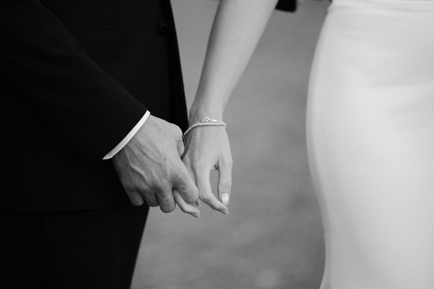 Black and white detail of groom holding bride’s hand during reception