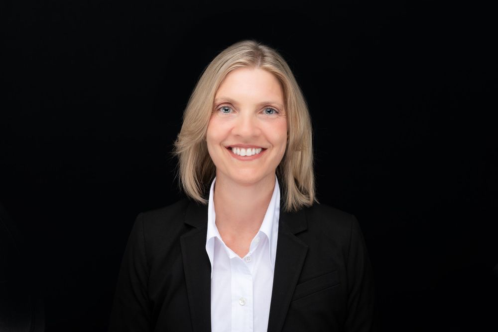 Professional headshot of someone in a black suit jacket against a dark backdrop.