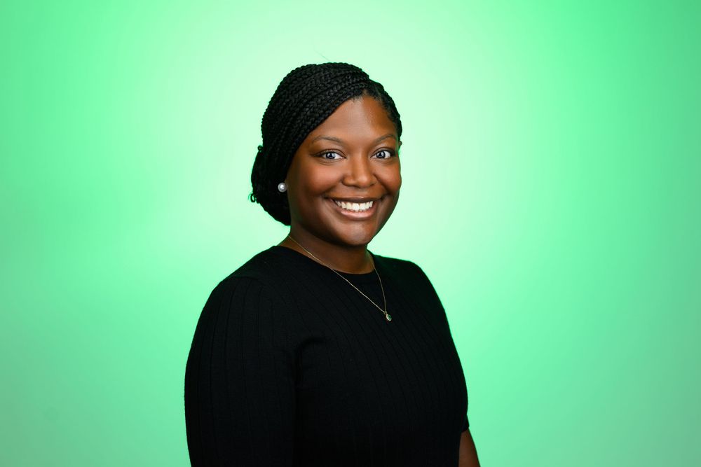 A person in black attire smiles warmly against a bright green background.