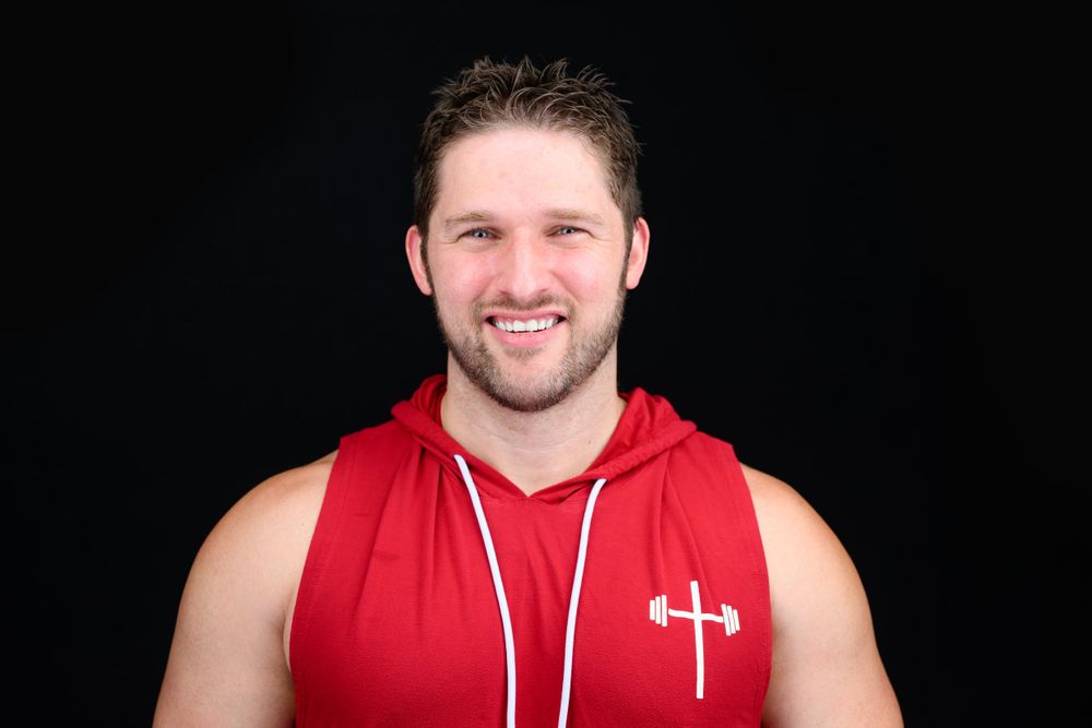 Professional portrait of someone in a red sleeveless hoodie against a black background.