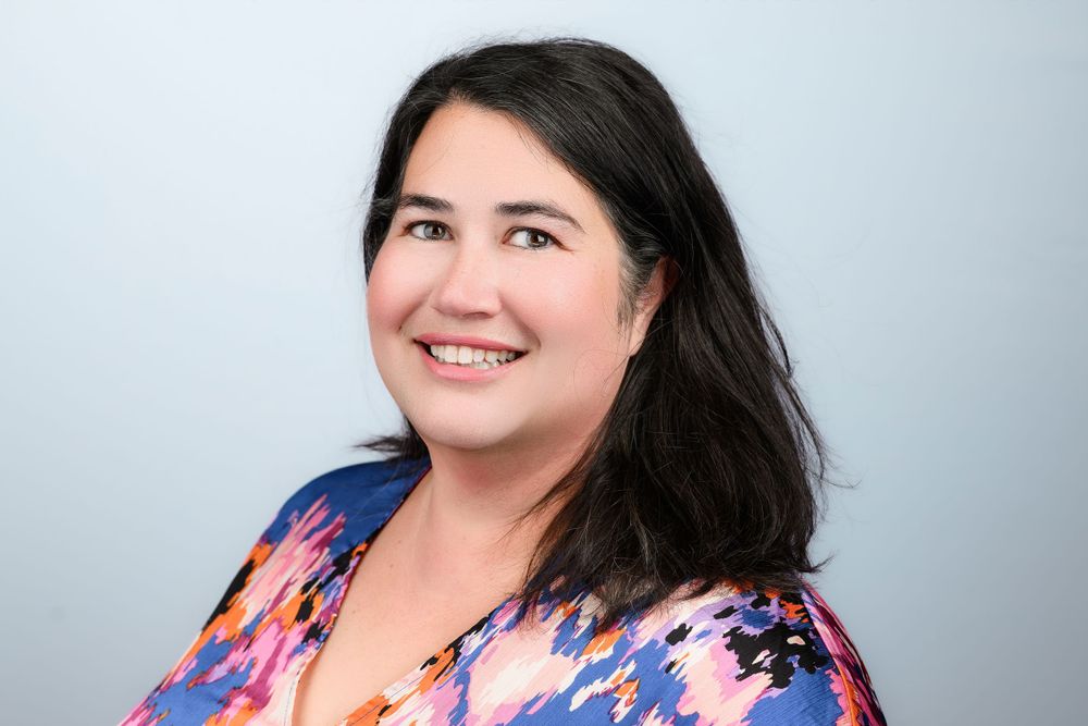 Professional headshot of woman in floral top against light gray background.