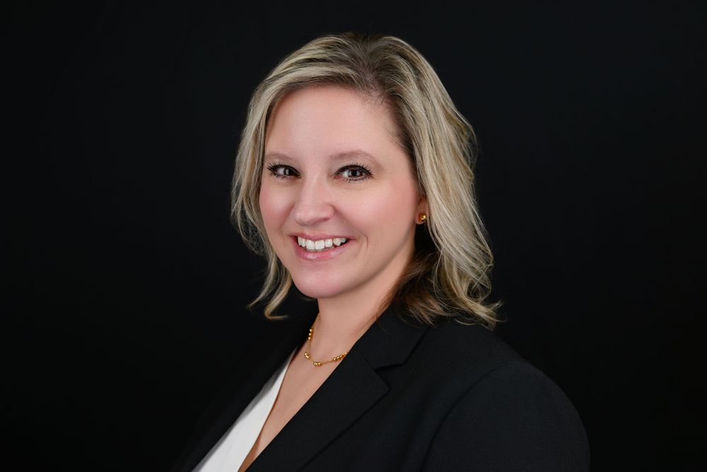 Professional headshot against black background with someone in dark blazer and blonde hair.