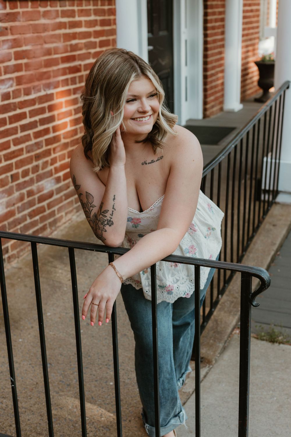 Person in white top leans on black metal railing in front of brick building.