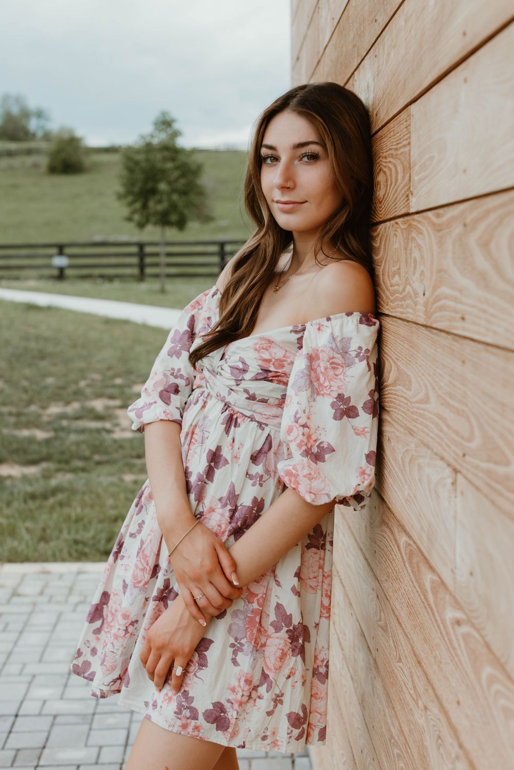 Woman in floral dress poses against beige wall in natural lighting.