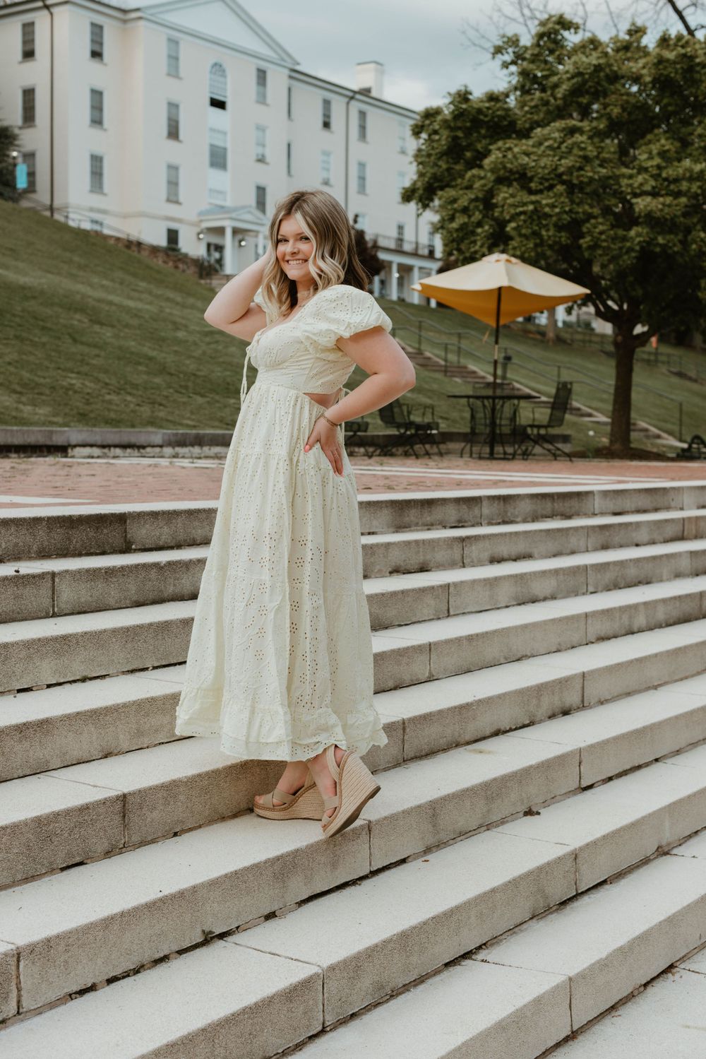 Person in flowing white dress poses on concrete steps near white building.