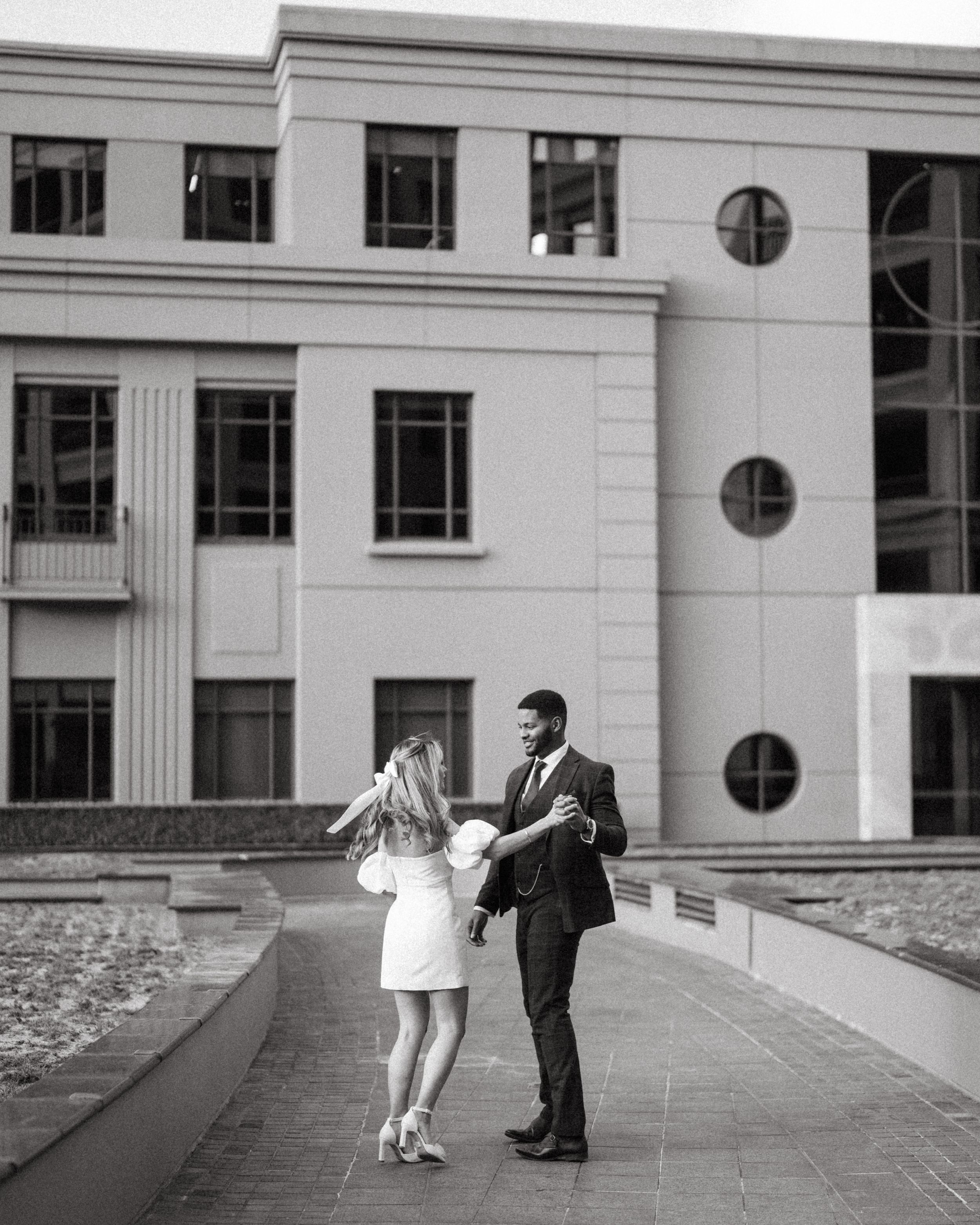 A couple shares a romantic moment on a walkway outside an art deco style building.