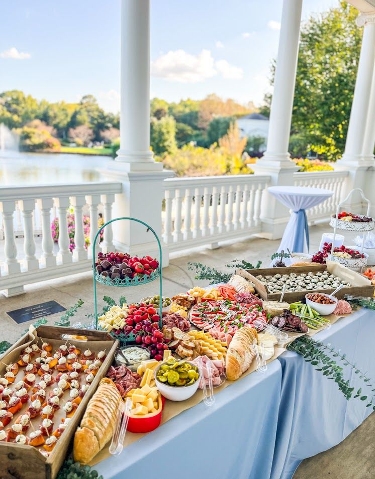 Elegant catering display with appetizers and snacks arranged on a white-columned porch overlooking autumn scenery.