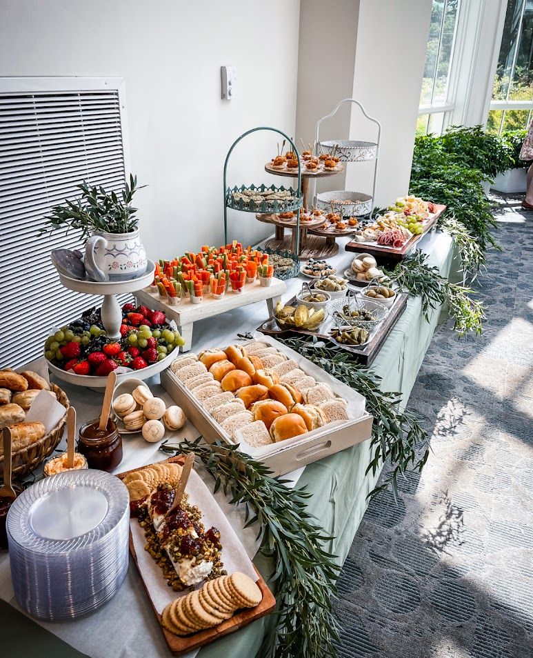 Modern grazing table with fresh fruits, crackers, and appetizers arranged on white surfaces with natural lighting.