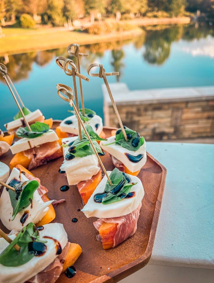 Gourmet appetizer bites served on wooden boards with decorative garnishes against a waterfront backdrop.