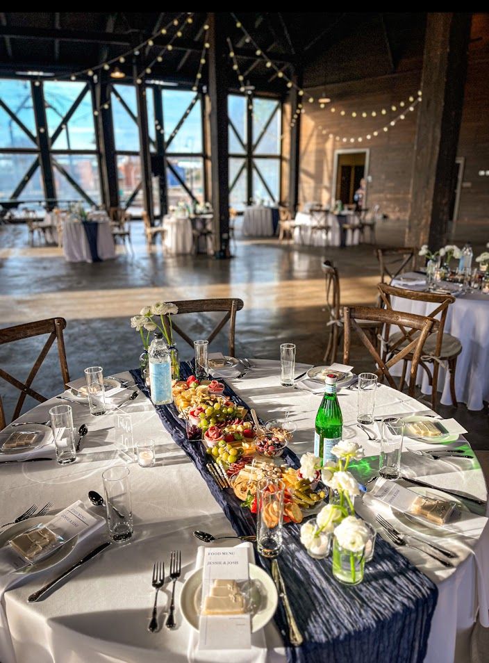 Formal table settings with navy blue runners and colorful charcuterie boards in an event space.