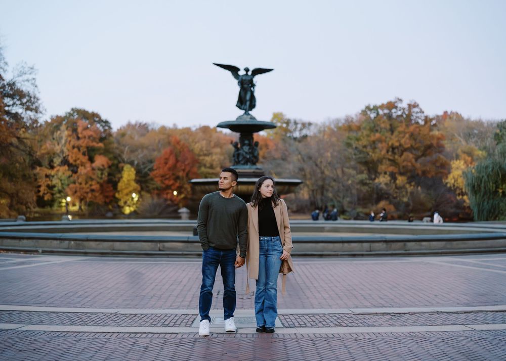 Couple poses before Bethesda Fountain in Central Park surrounded by fall foliage at dusk.