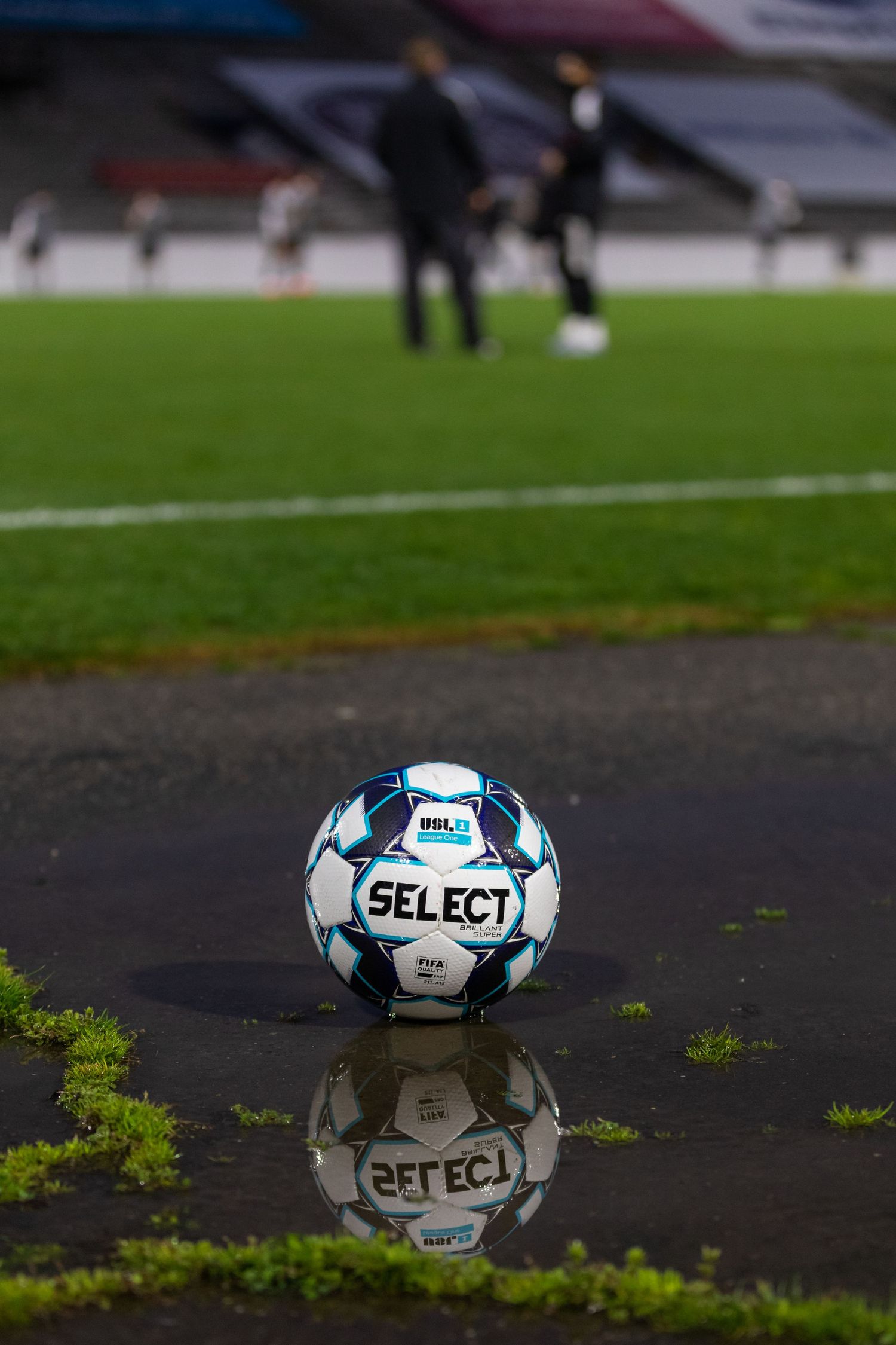 Select brand soccer ball reflecting on wet pavement with blurred background.