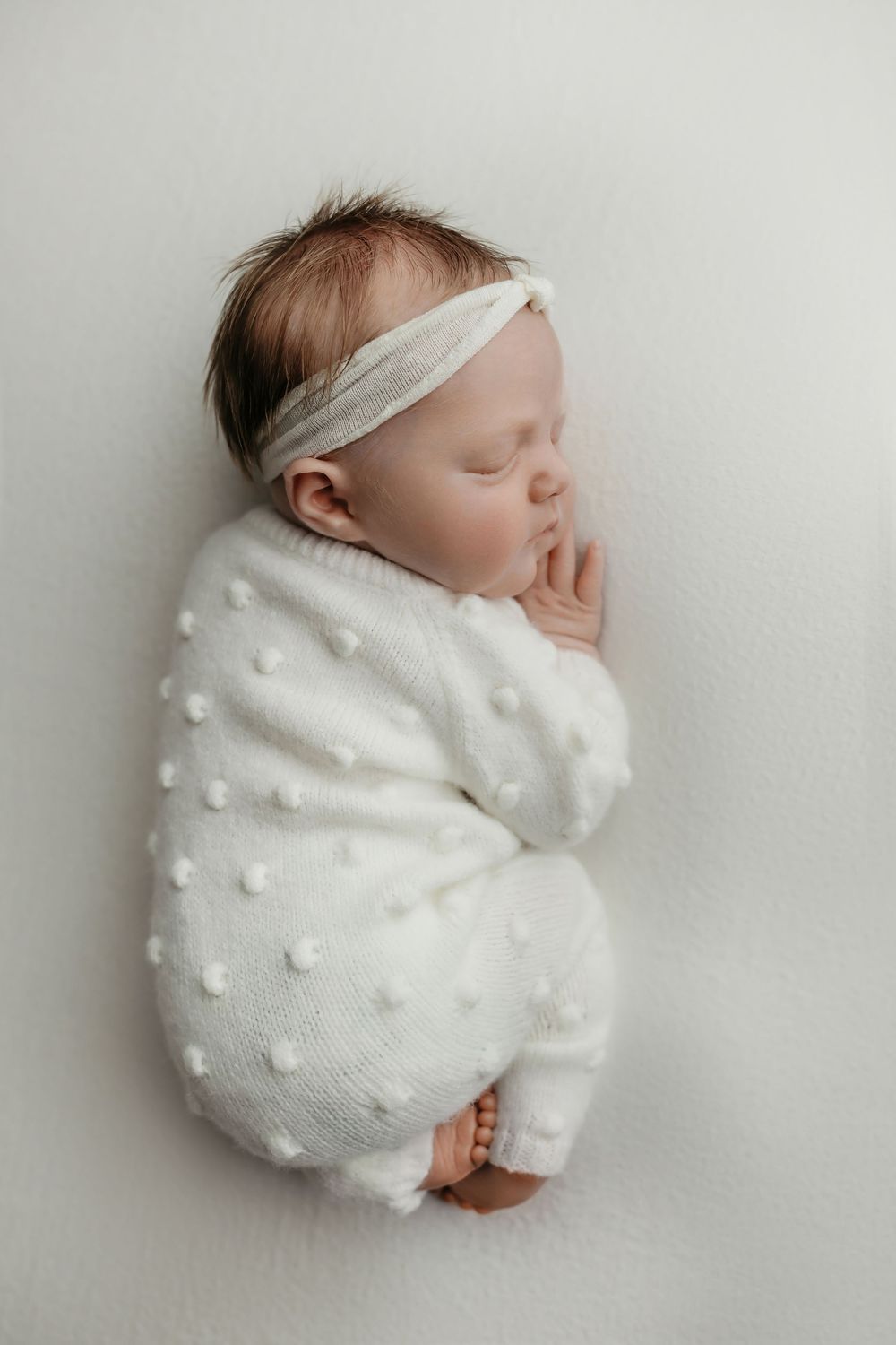Newborn girl on white background in white jumper, taken by Jen Knightstep, Photographer