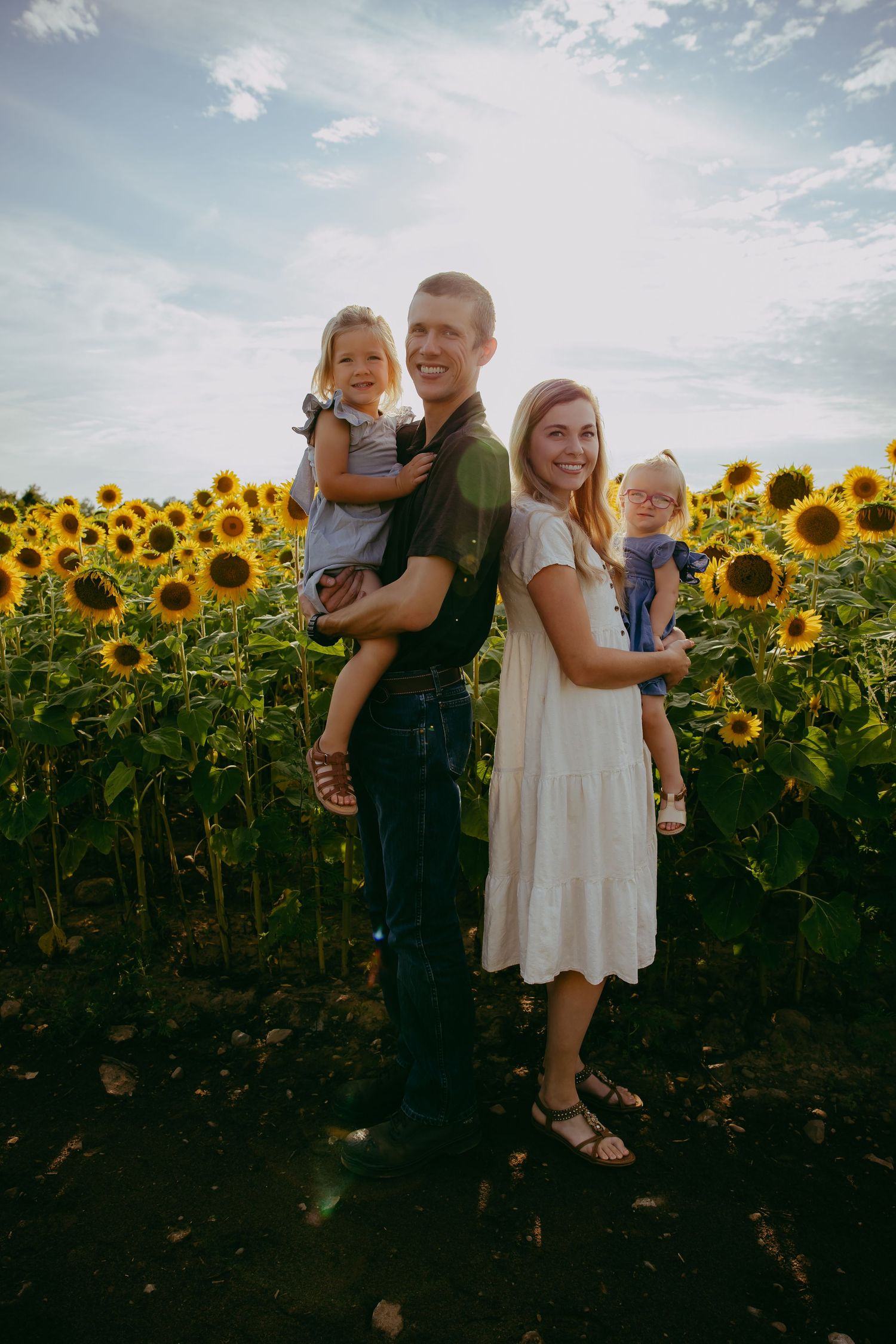 Family standing together in a vibrant sunflower field at sunset.