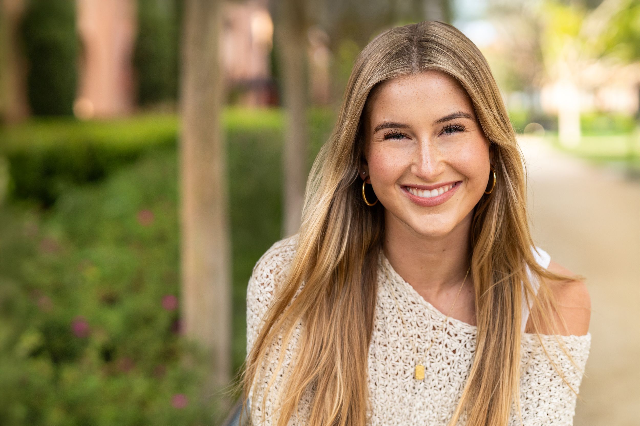 A professional headshot photo of someone in business attire against a bright outdoor background.