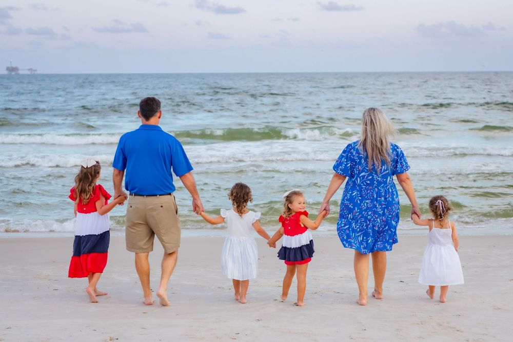 A group walks together holding hands along a white sandy beach with blue ocean waves in the background.