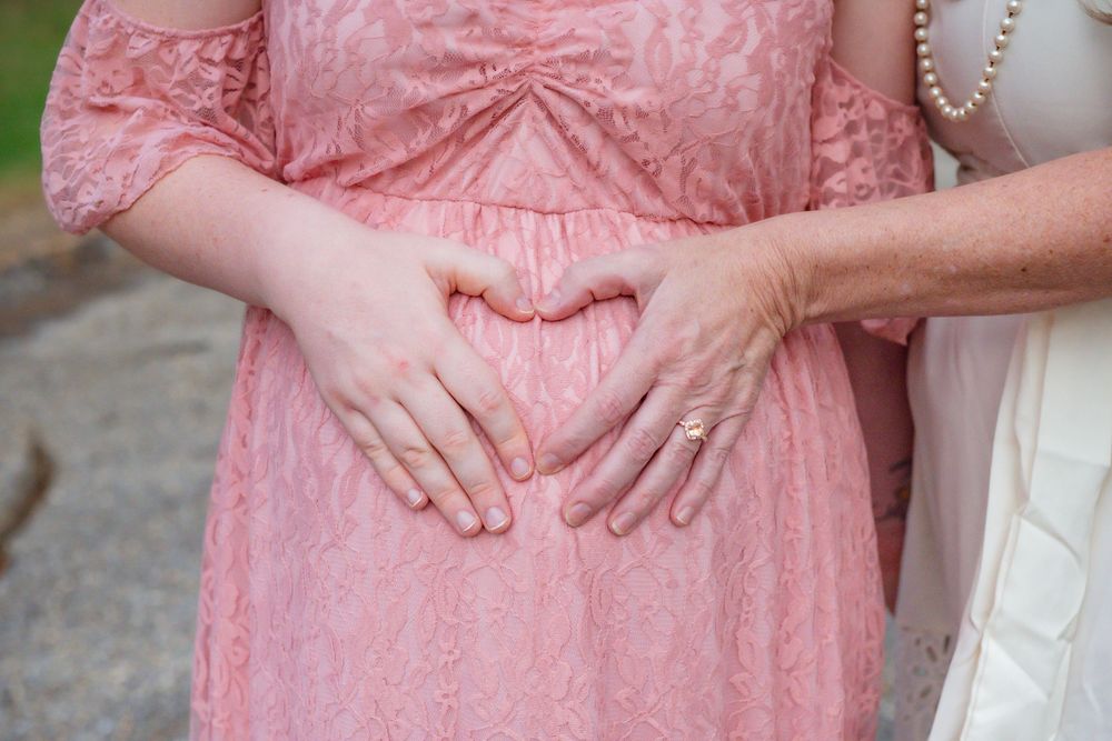 Hands form a heart shape over a pink lace dress, showing a tender gesture during a special moment.