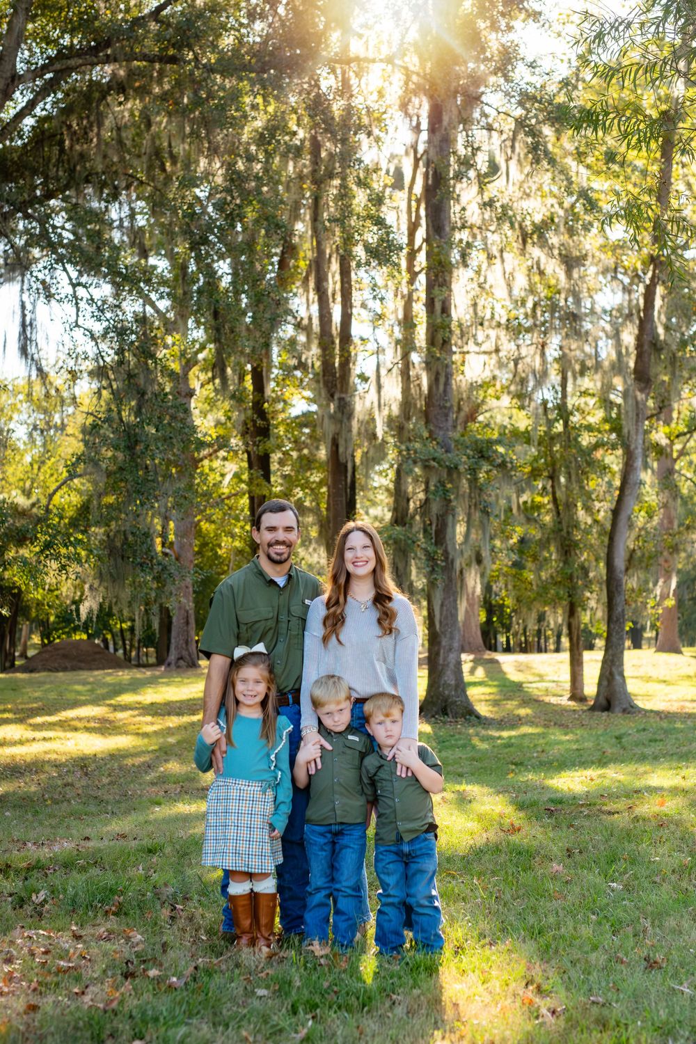 A family poses together in a sunlit wooded area during golden hour with Spanish moss hanging from trees.