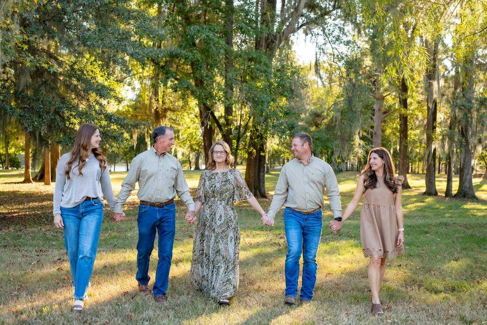 A group walks together through a sunlit wooded area during a casual outdoor photo session.