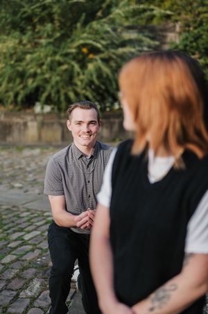 Professional outdoor photoshoot session with two people conversing on stone pavement surrounded by lush greenery.
