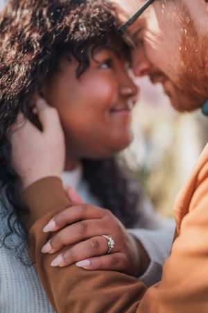 Close up of a romantic couple sharing an intimate moment while showing off a diamond engagement ring.