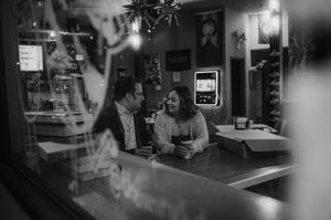 A black and white panoramic view of a dimly lit bar interior with vintage decor and empty barstools.