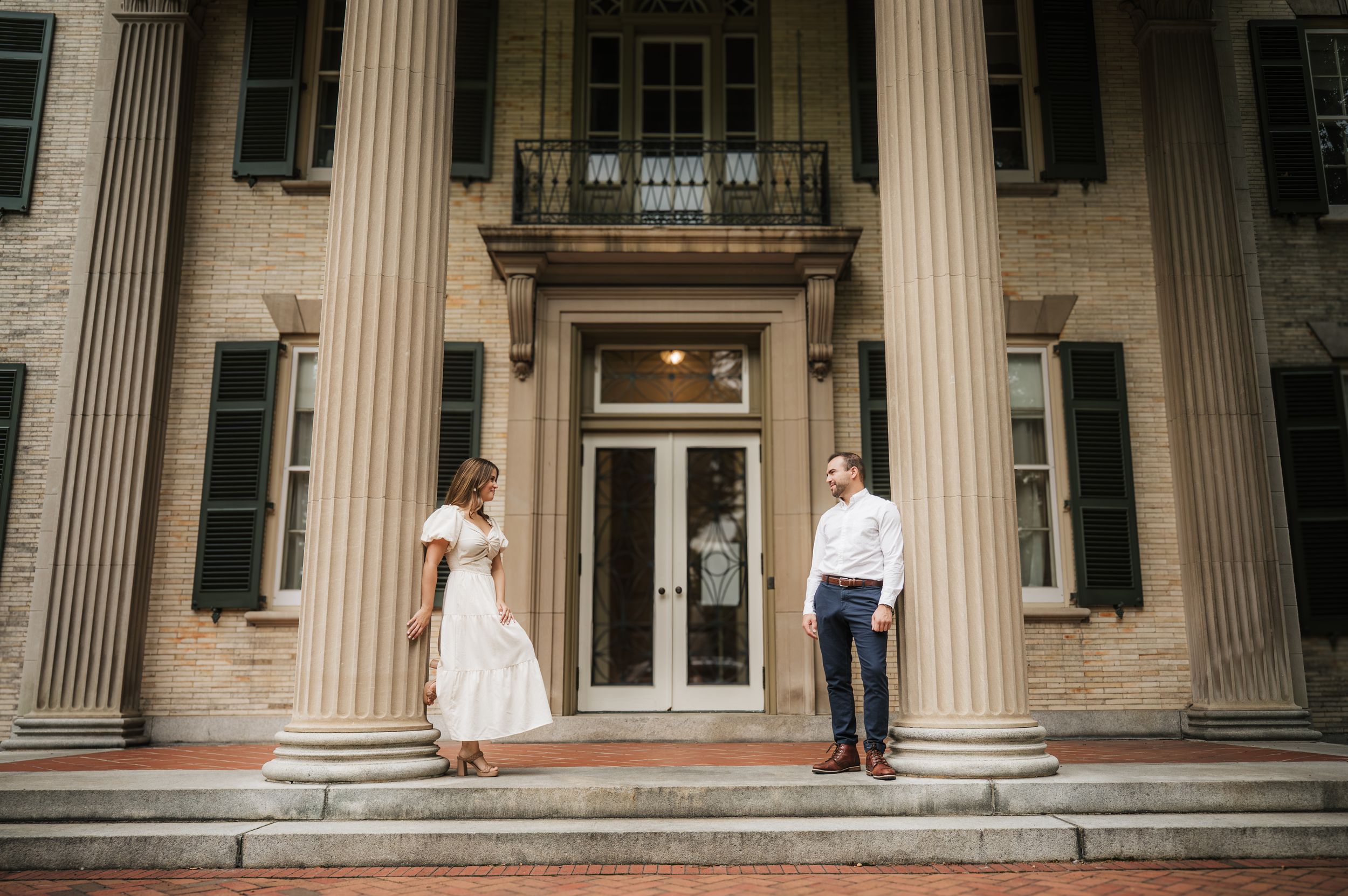 A grand building exterior with tall white columns and stone architecture makes an elegant backdrop for a wedding photo.