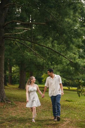 A couple in white clothing walks together through a lush green park on a summer afternoon.