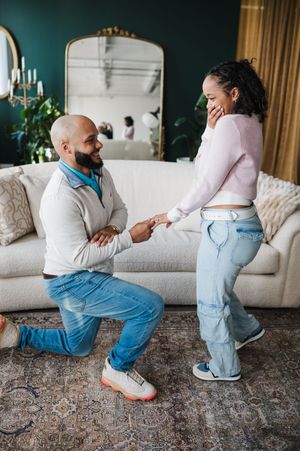 A heartfelt proposal moment between a couple in their living room with a white couch and teal walls.