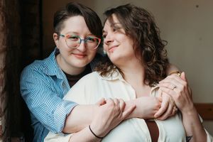 Close up couple sharing intimate embrace wearing casual attire in a light filled indoor setting.