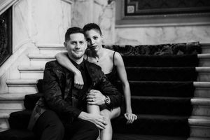 A black and white portrait of a couple sitting intimately together on marble stairs indoors.