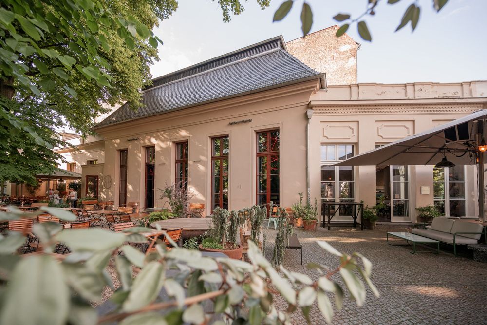 Historic building exterior with outdoor seating area and green foliage in foreground.