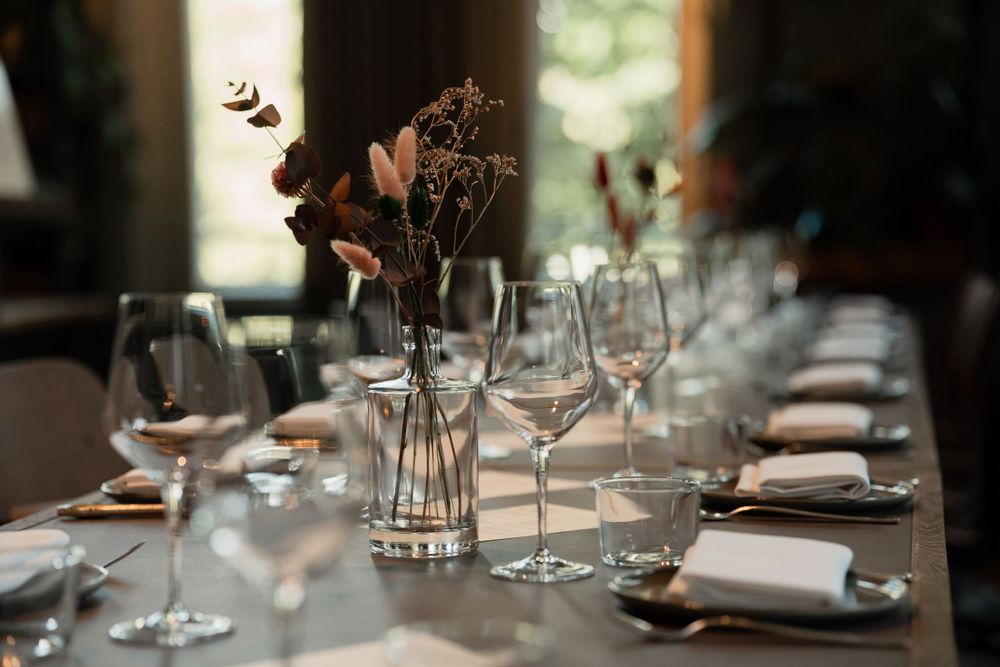 Elegant table setting with wine glasses and dried flower centerpiece in muted lighting.