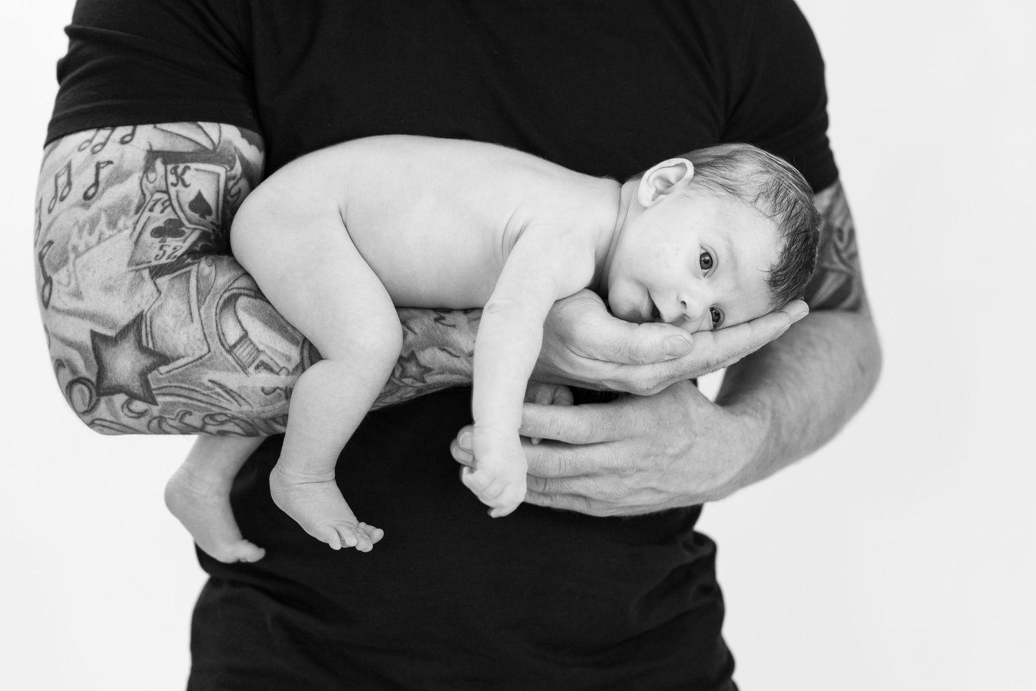 Nyfødt baby ligger trygt i fars tatoverede arme – newborn fotografering i Jægerspris, Frederikssund og Nordsjælland